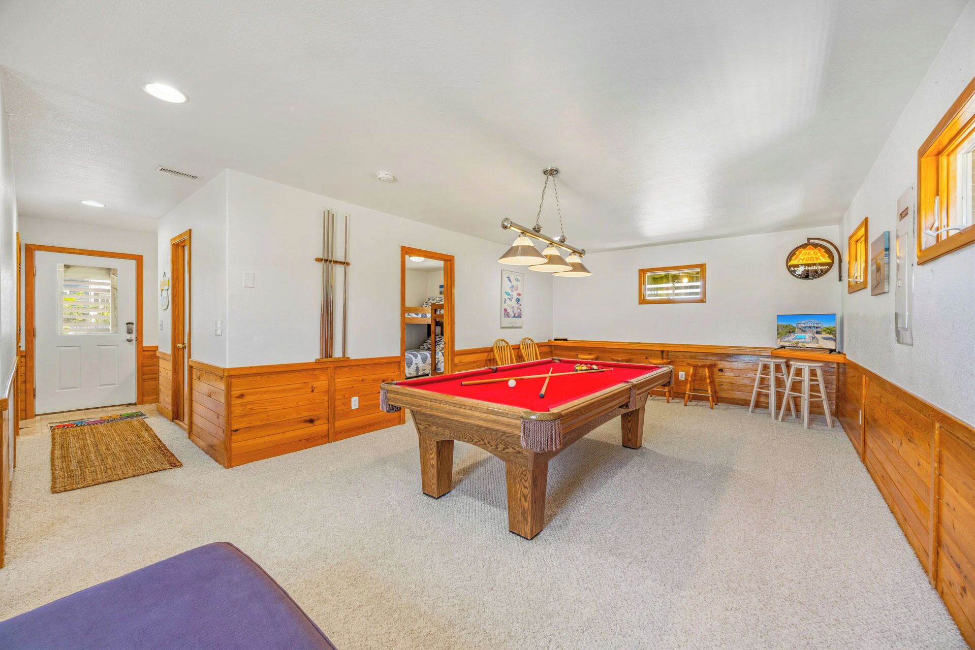 A pool table in a room with wooden paneling, a bar area, and a door leading to another room.