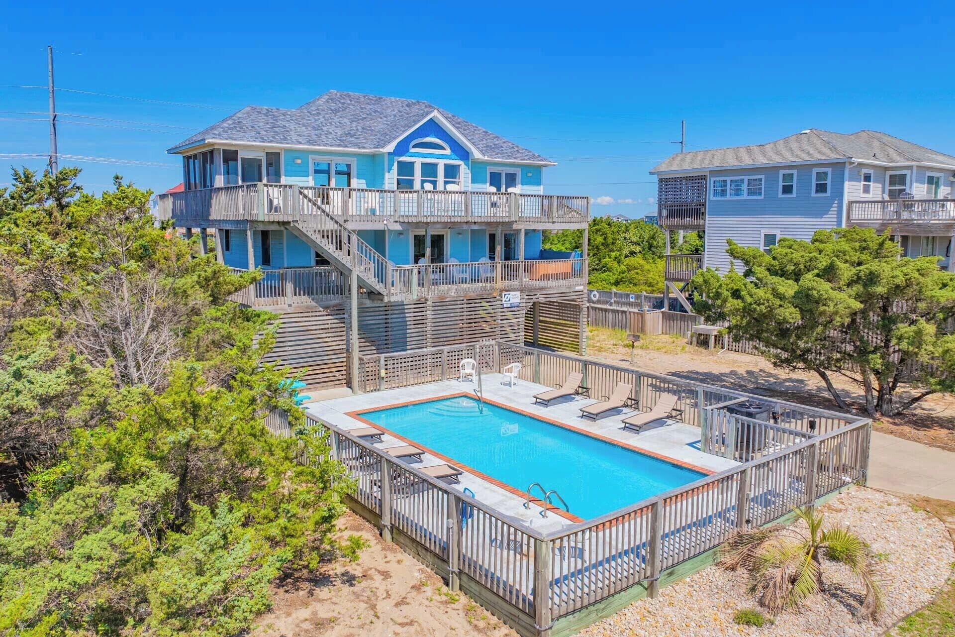 Een strandhuis met zwembad, houten terras en een twee verdiepingen tellend gebouw met balkon.