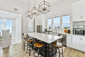 A modern kitchen with white cabinetry, a large island with stools, and pendant lighting.