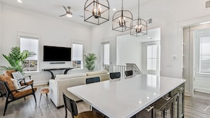 A spacious living area with a large white island, a sofa, and a TV mounted on the wall. - Modern & cozy home with balcony, patio, washer/dryer, pool access, kitchen, WiFi (Port Aransas)