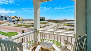 A porch with white railings and a table, overlooking a beach area with buildings and a road. - Modern & cozy home with balcony, patio, washer/dryer, pool access, kitchen, WiFi (Port Aransas)