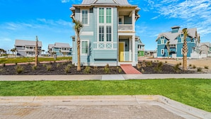 A two-story residential building with a balcony, surrounded by a well-maintained lawn and palm trees. - Modern & cozy home with balcony, patio, washer/dryer, pool access, kitchen, WiFi (Port Aransas)