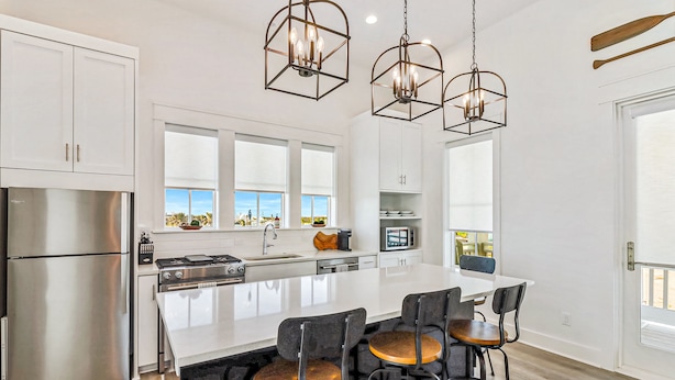 A modern kitchen with white cabinetry, stainless steel appliances, a large island with bar stools, and pendant lighting. - Modern & cozy home with balcony, patio, washer/dryer, pool access, kitchen, WiFi (Port Aransas)
