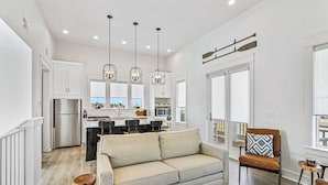 A modern kitchen with white cabinets, a central island, and pendant lighting. - Modern & cozy home with balcony, patio, washer/dryer, pool access, kitchen, WiFi (Port Aransas)