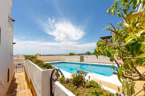 A swimming pool surrounded by a white wall and plants, with a clear blue sky above.
