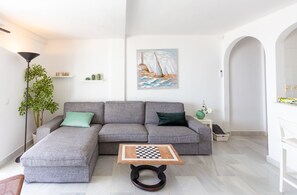 A modern living room with a grey sectional sofa, a small wooden coffee table with a chessboard, a floor lamp, and a painting of a sailboat on the wall.