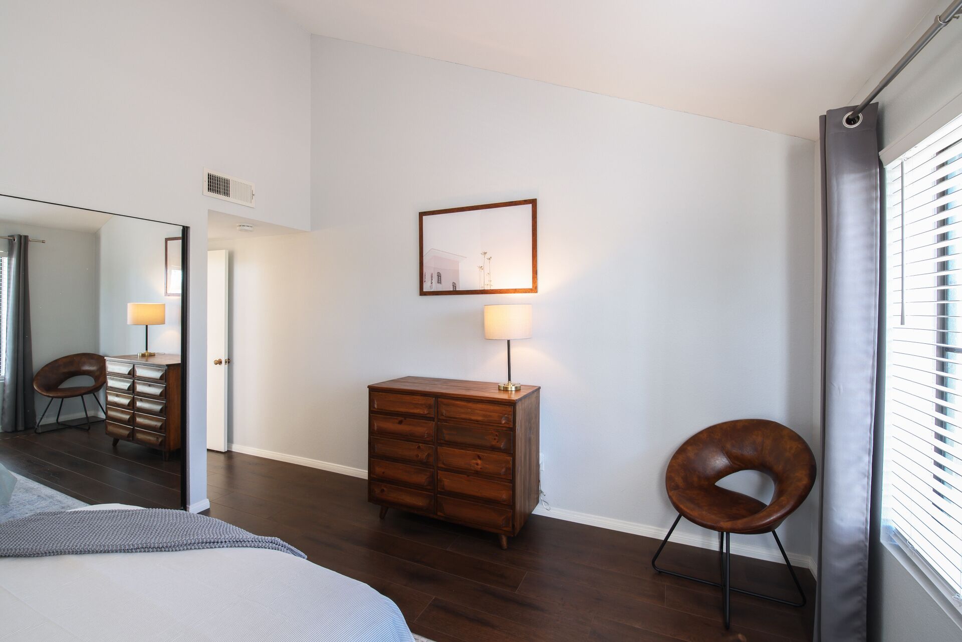 Ein modernes Schlafzimmer mit einem Bett, einer Holzkommode, einem Stuhl und einem gerahmten Bild an der Wand.