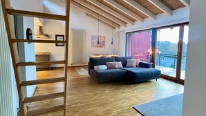 Un loft espacioso con piso de madera, sofá integrado y un ventanal con vistas al exterior.
