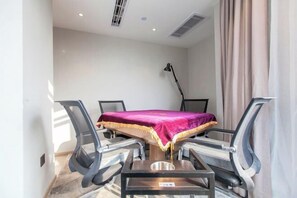 Une salle de conférence avec une table, quatre chaises, une nappe rouge, un lampadaire et une fenêtre avec des rideaux.