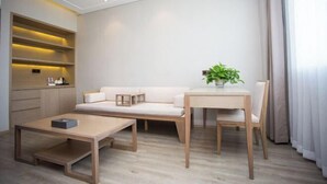 A modern living room with a sofa, a wooden coffee table, a small table with a plant, and built-in shelving. - Jiasheng International Hotel (Jiayu)