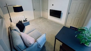 Olohuone, jossa on sohva, seinälle asennettu televisio, lamppu ja ovi.