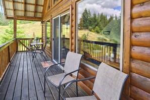 A wooden deck with two chairs and a small table, overlooking a forested area.