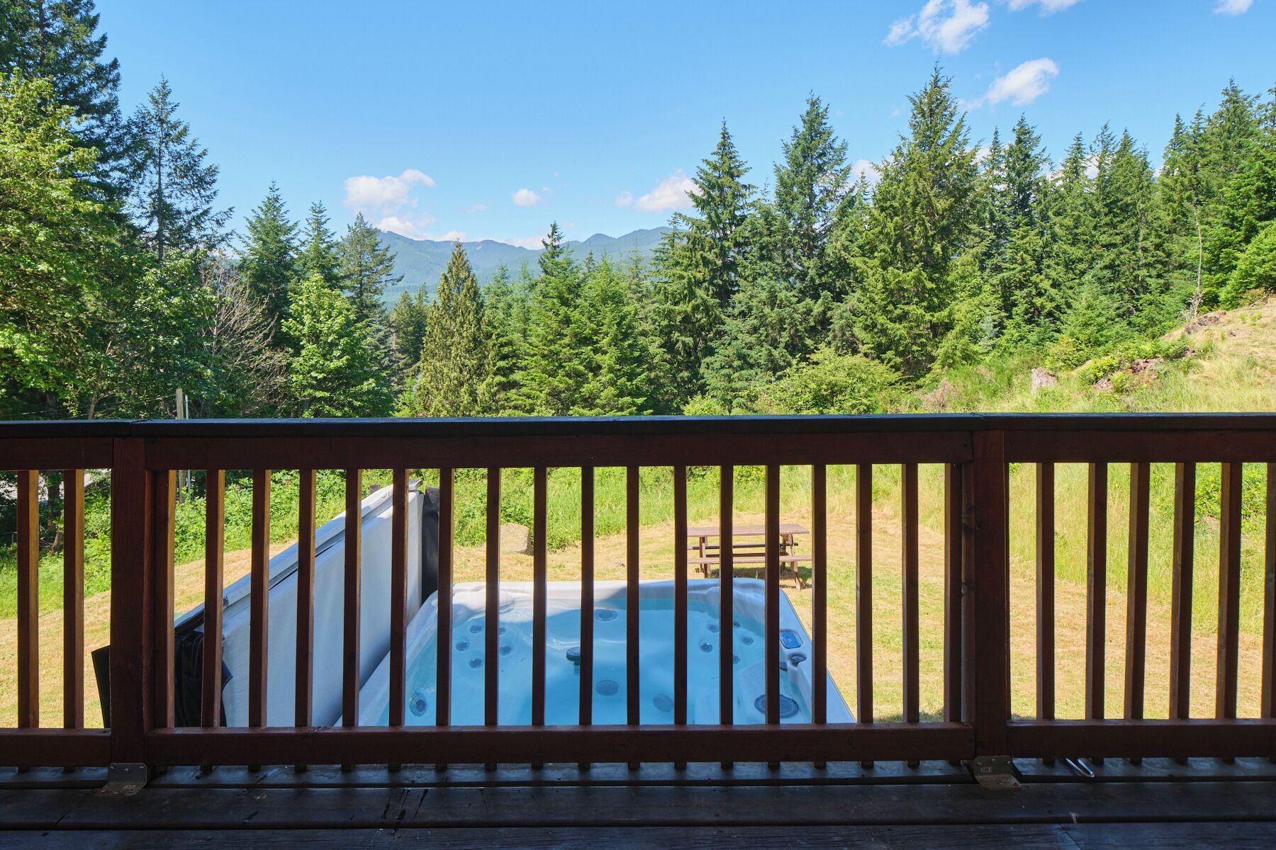 Un jacuzzi rodeado por una terraza de madera con vistas a un bosque y montañas.