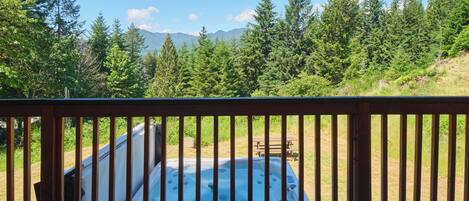 Un jacuzzi rodeado por una terraza de madera con vistas a un bosque y montañas.