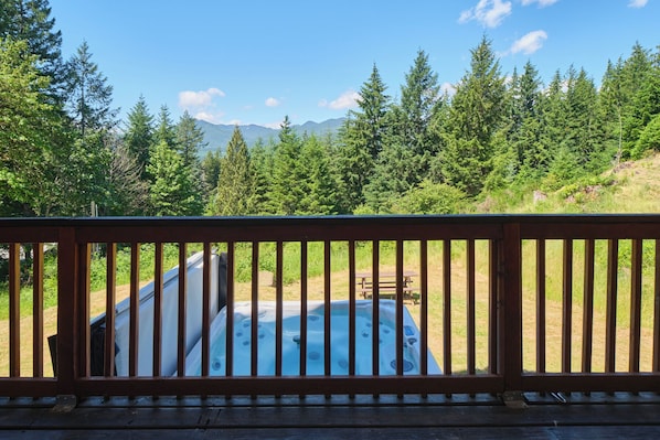 A hot tub surrounded by a wooden deck with a view of a forest and mountains.