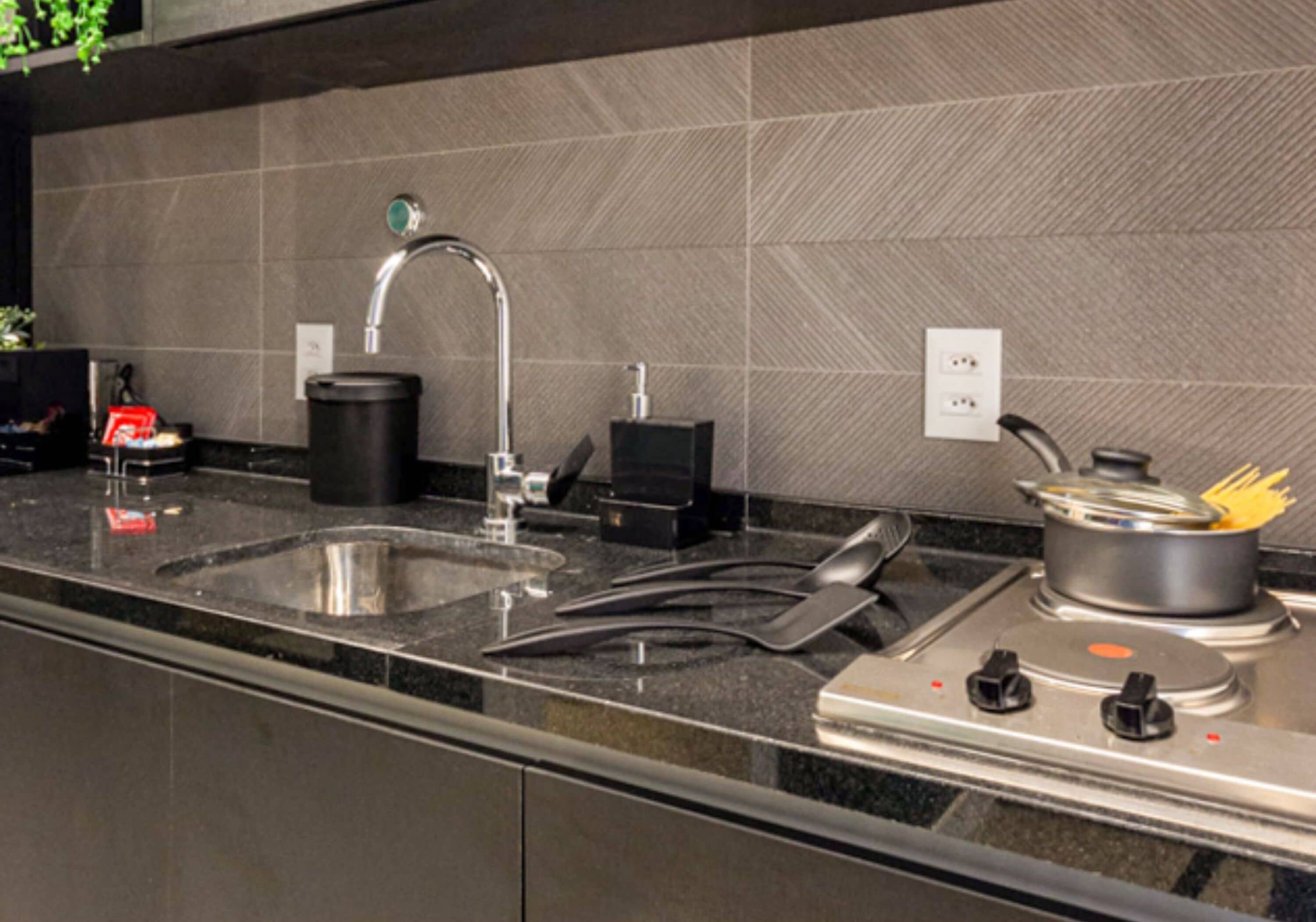 Una cucina moderna con lavello in acciaio inox, macchina del caffè e fornello con pentole.