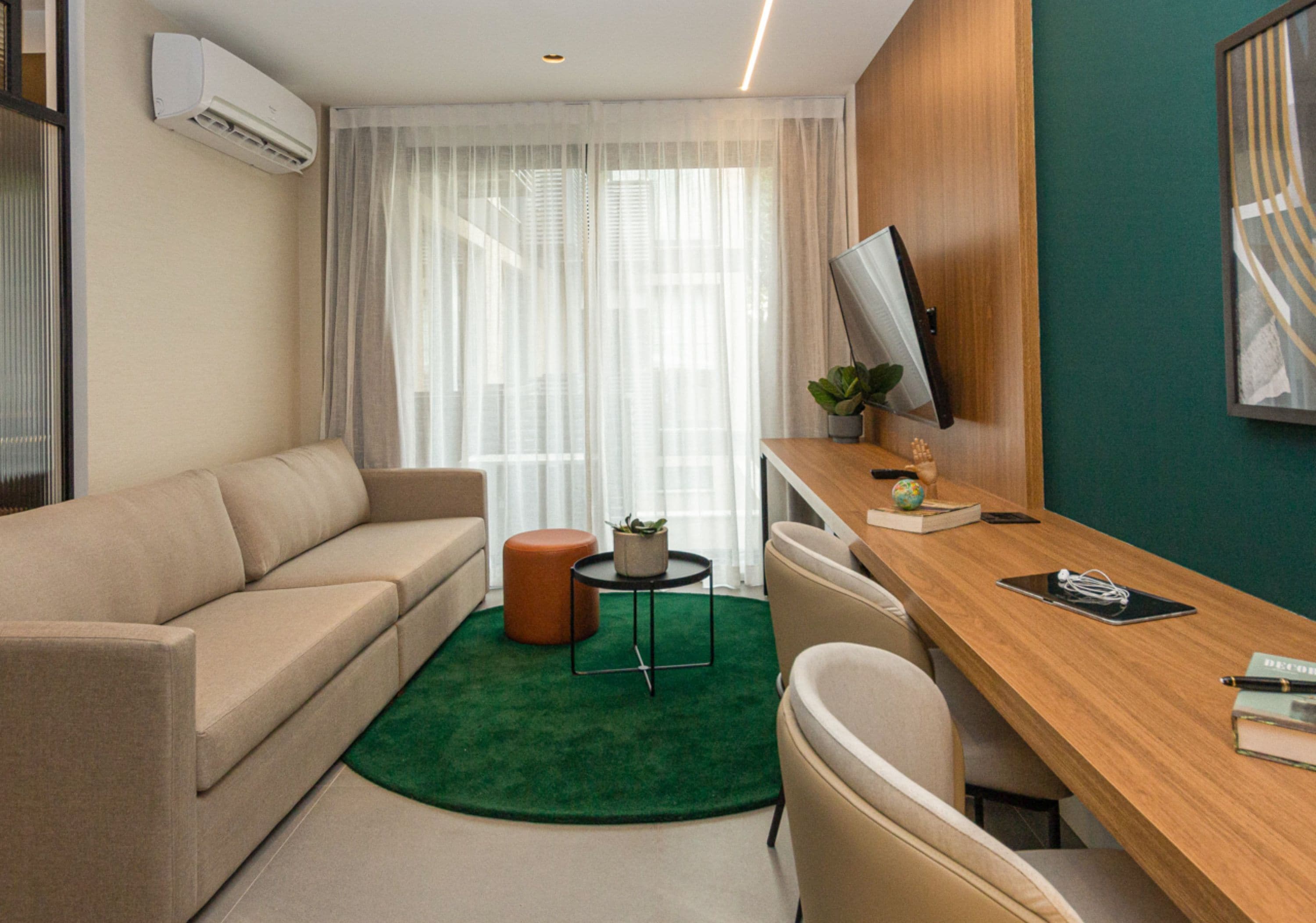 Een moderne hotelkamer met een bank, een bureau, een klein tafeltje met een plant en een televisie aan de muur.