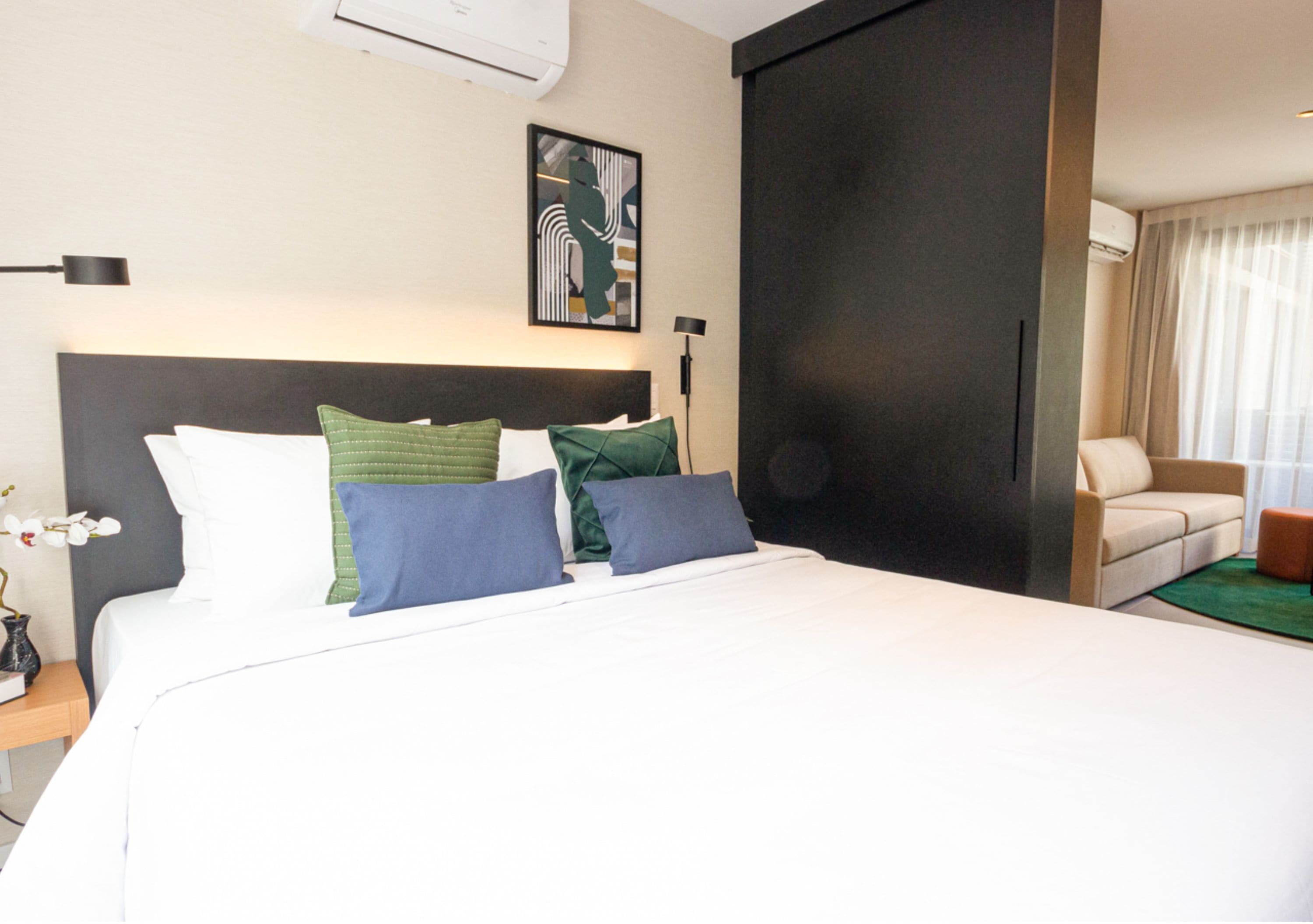 A hotel room with a large bed, a desk with a lamp, a chair, and a window with curtains.