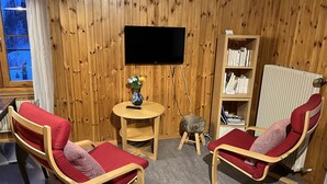 A cozy room with wooden walls, a flat-screen TV, a small round table with a vase, two red cushioned chairs, a bookshelf, and a radiator. - In the village of Evolène friendly sunny studio (Evolène)