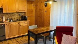 A compact kitchen with wooden cabinets and a dining area with a red chair and table. - In the village of Evolène friendly sunny studio (Evolène)