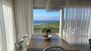 A dining area with a view of the ocean, featuring a wooden table, white chairs, and a vase with flowers.