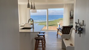 A modern kitchen with a large island, bar stools, a dining area with a view of the ocean, and a seating area with a view of the beach.