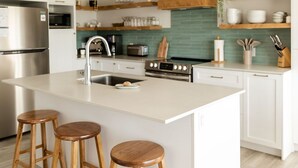 A modern kitchen with a central island, wooden stools, white cabinetry, and stainless steel appliances.