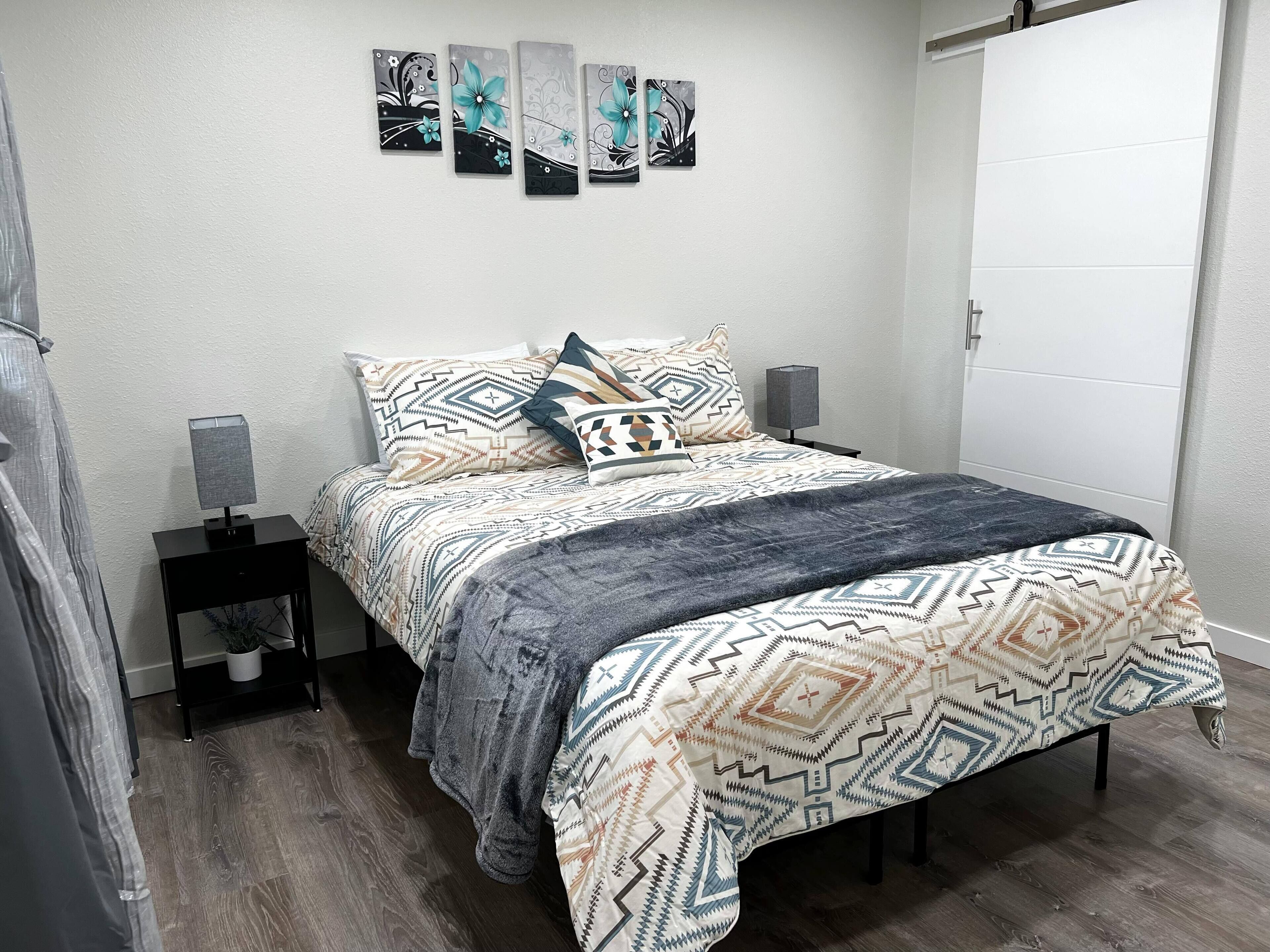 A modern bedroom with a bed, patterned bedding, a bedside table with a lamp, and wall art.