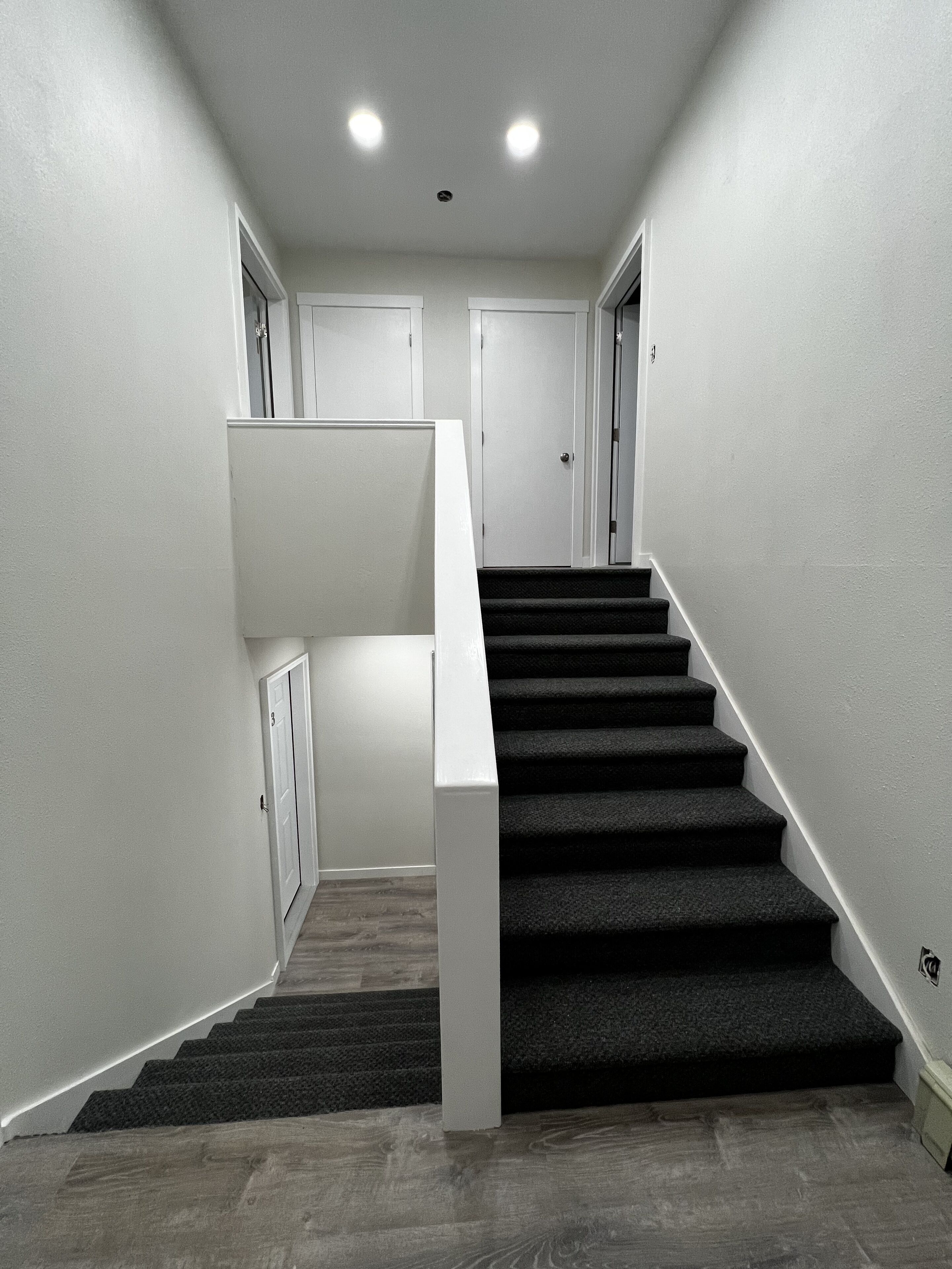 Una escalera moderna con barandilla blanca y peldaños alfombrados, que conduce a una plataforma con una puerta y un armario pequeño.
