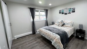 Een slaapkamer met een bed, een raam met gordijnen, een nachtkastje met een lamp en een muur met kunstwerken.