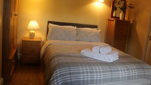 Un dormitorio con cama, una mesita de noche con lámpara, cómoda y espejo.