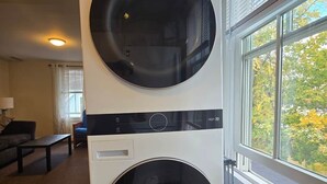 Une machine à laver et un sèche-linge superposés, placés dans une pièce avec une fenêtre donnant sur la vue des arbres à l’extérieur.
