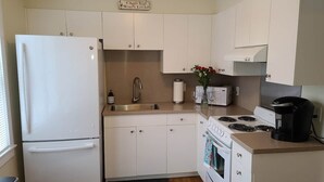 Une cuisine de taille réduite avec des meubles blancs, un réfrigérateur, un évier, une cuisinière et une machine à café.