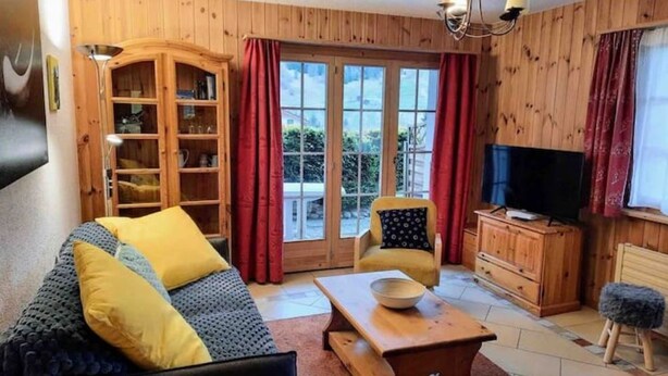 Un salon confortable avec un canapé, un téléviseur, un meuble en bois et une grande fenêtre avec des rideaux.