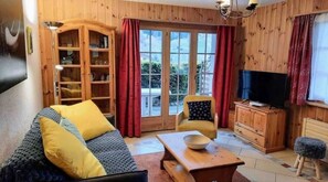 A cozy living room with a sofa, a television, a wooden cabinet, and a large window with curtains. - L'Herensarde, apartment with terrace and garage (Evolène)