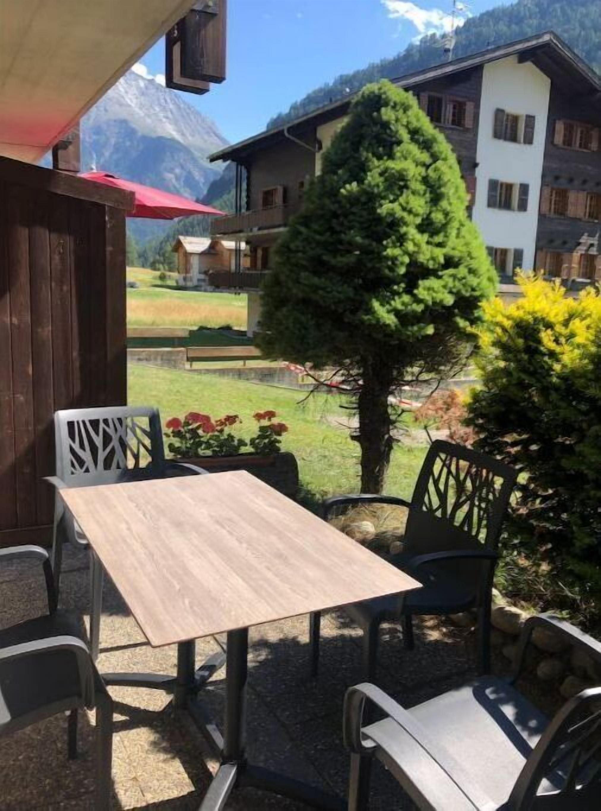Uma área de estar externa com mesa, cadeiras, um vaso de planta e vista para uma montanha ao fundo.
