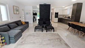 Un salon moderne avec un canapé gris, deux fauteuils noirs, une table basse et un coin repas comprenant une table et des chaises en bois.