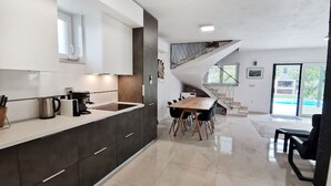 Une cuisine moderne avec des meubles de couleur sombre, un plan de travail blanc et un coin repas comprenant une table et des chaises en bois.