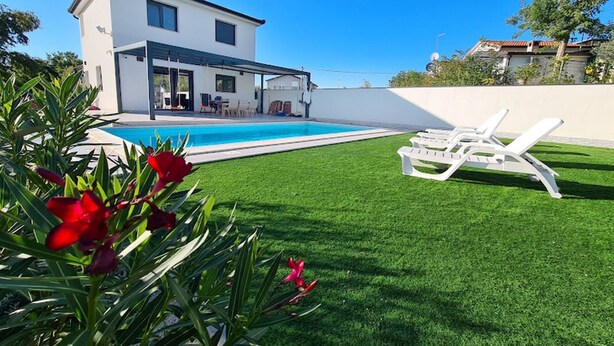 Une maison moderne dotée d’une piscine, d’une pelouse et de chaises longues blanches.