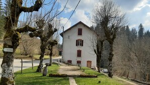 Un bâtiment blanc aux volets rouges, entouré d’arbres et d’une zone herbeuse.