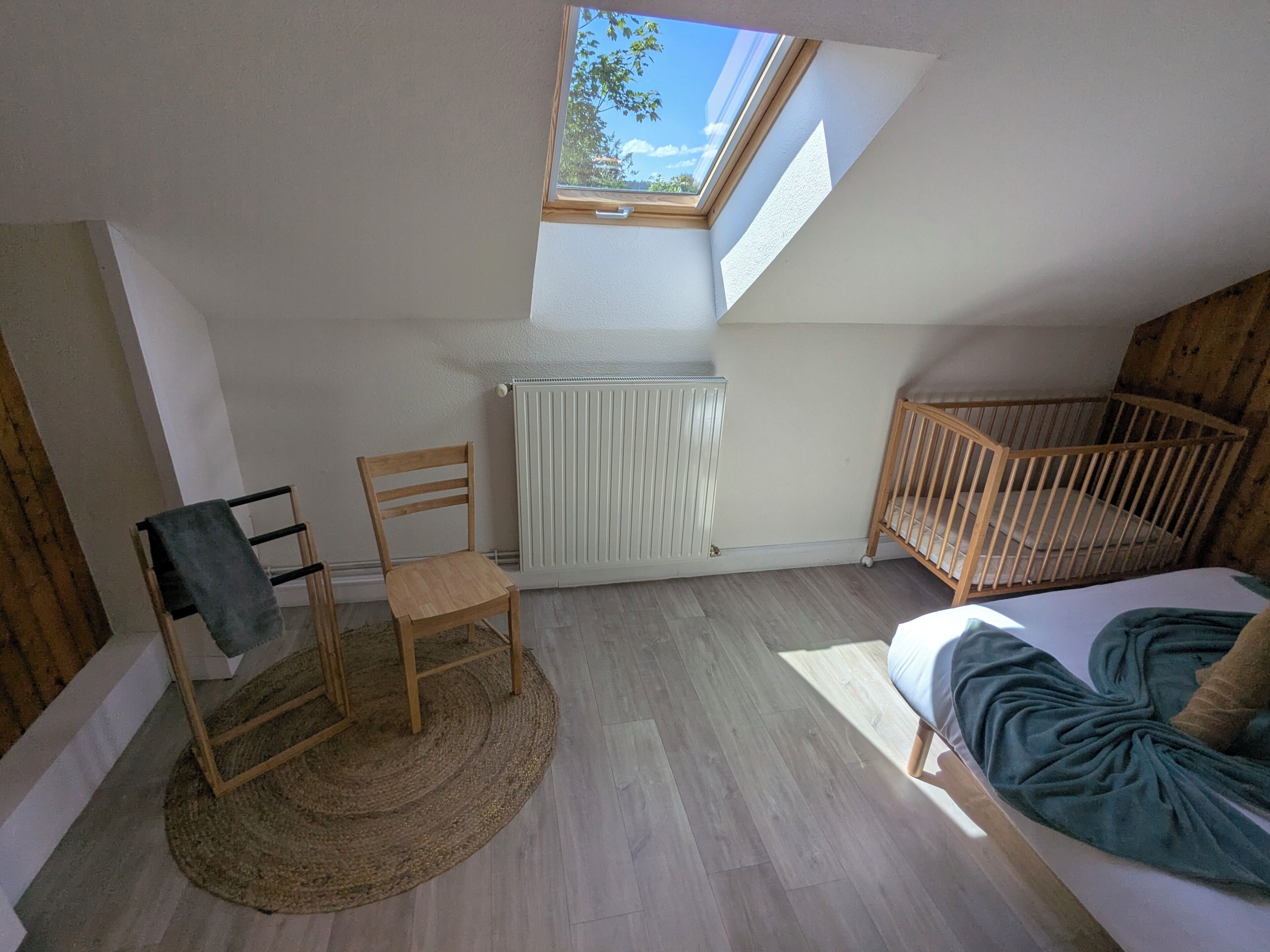 A room with a sloped ceiling, a wooden crib, a rocking chair, a radiator, and a skylight.