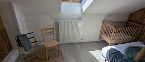 A room with a sloped ceiling, a wooden crib, a rocking chair, a radiator, and a skylight.