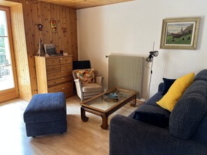 A cozy living room with wooden walls, a sofa, a chair, a coffee table, and a dresser.
