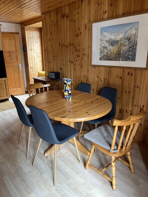 A wooden-paneled room with a round wooden table surrounded by chairs, a painting on the wall, and a wooden cabinet.