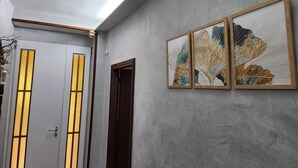Een gang met een witte deur met verticale gouden patronen, een houten deur en drie ingelijste kunstwerken aan de muur.