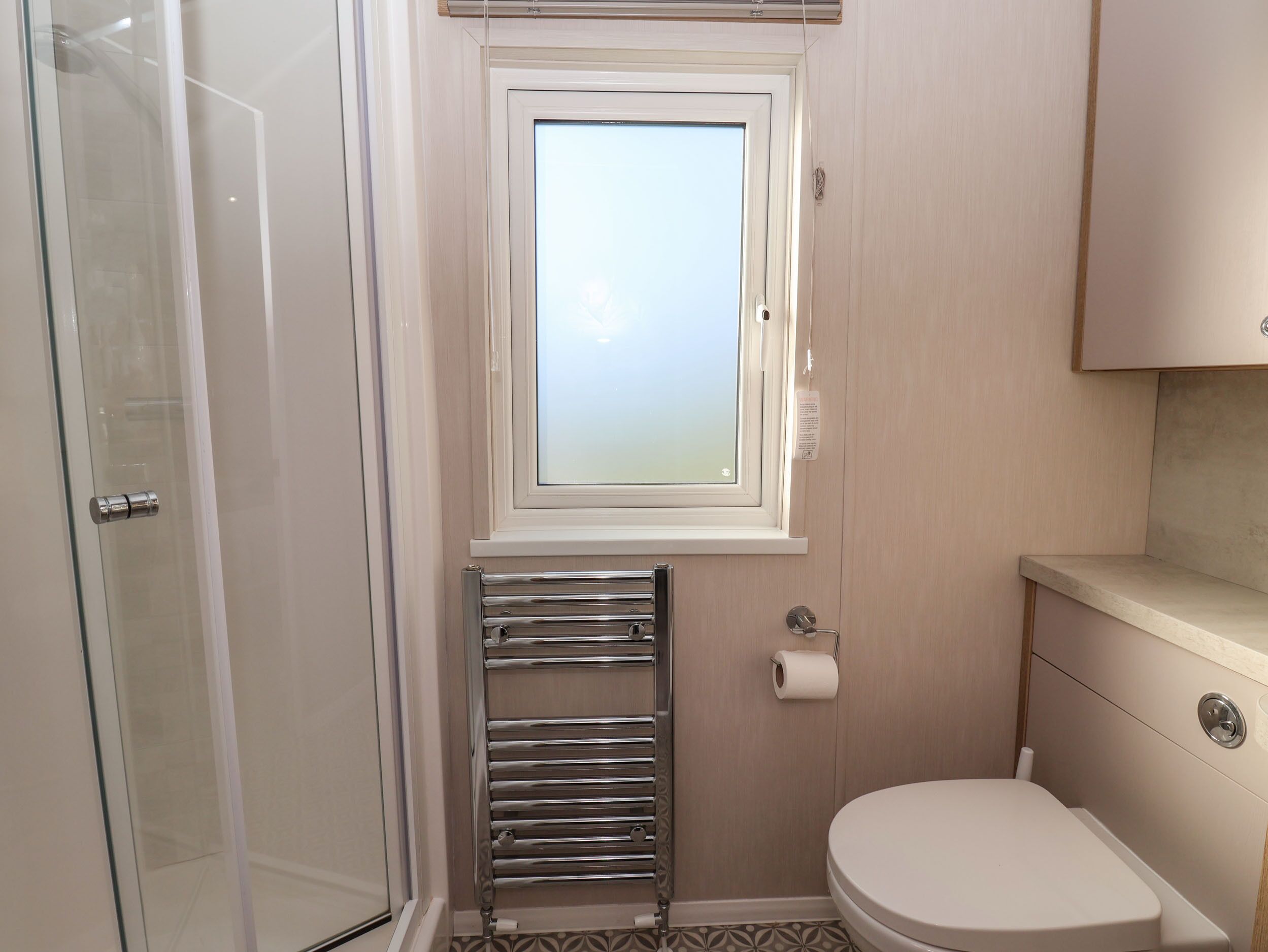 A bathroom with a glass shower enclosure, a toilet, a towel rack, and a window.