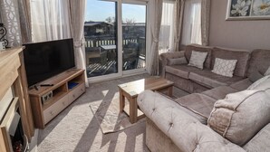 A living room with a TV, sofa, and a view through glass doors to a balcony. - Owls Nest (York)
