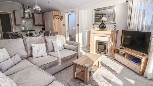 A modern living room with a sofa, coffee table, fireplace, TV, and kitchen area. - Owls Nest (York)