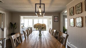 A dining room with a wooden table, chairs, a vase of flowers, and framed botanical prints on the wall. - Riverfront Shore House w/ Ocean View, Private Beach, 6 Bedrooms and Lots of Toys (Brielle)