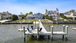 A waterfront property with a dock, chairs, and a flag. - Riverfront Shore House w/ Ocean View, Private Beach, 6 Bedrooms and Lots of Toys (Brielle)